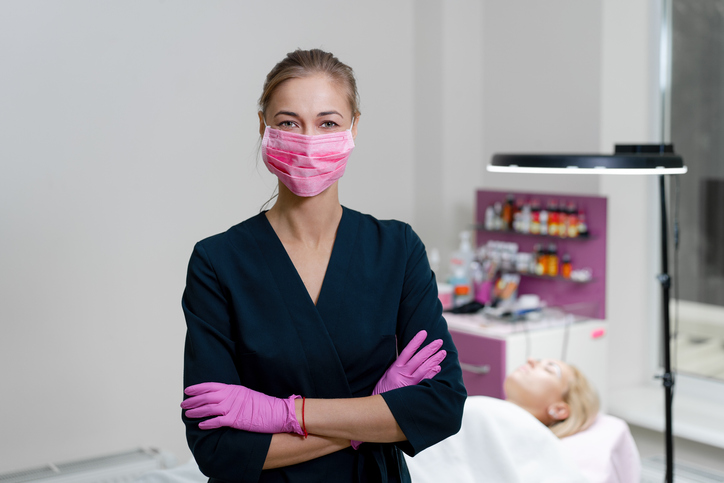 Beautician stands in pink medical mask and smiles. Preparation for the procedure of permanent eyebrow makeup.